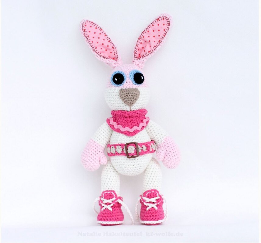 Gehäkelter weiß-rosa Amigurumi-Hase mit gepunkteten Ohren und pinken Schnürschuhen auf hellem Hintergrund