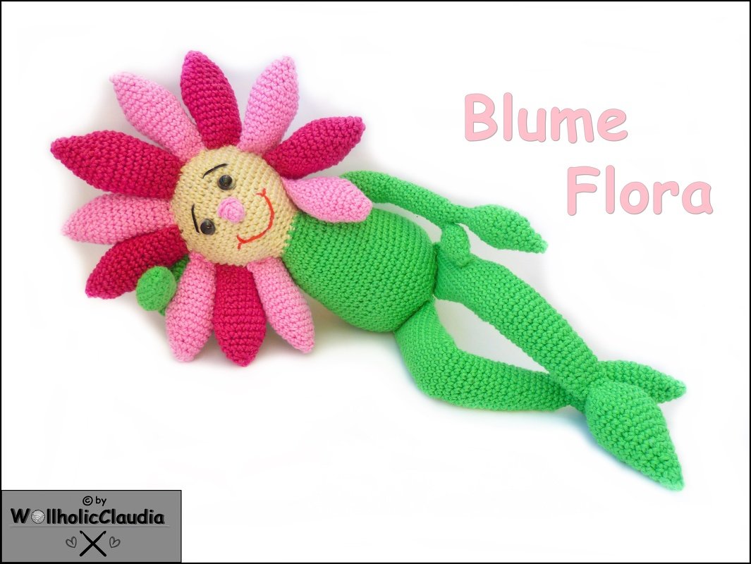 Gehäkeltes Blumen-Amigurumi mit rosa und pinken Blütenblättern, grünem Körper und lächelndem Gesicht