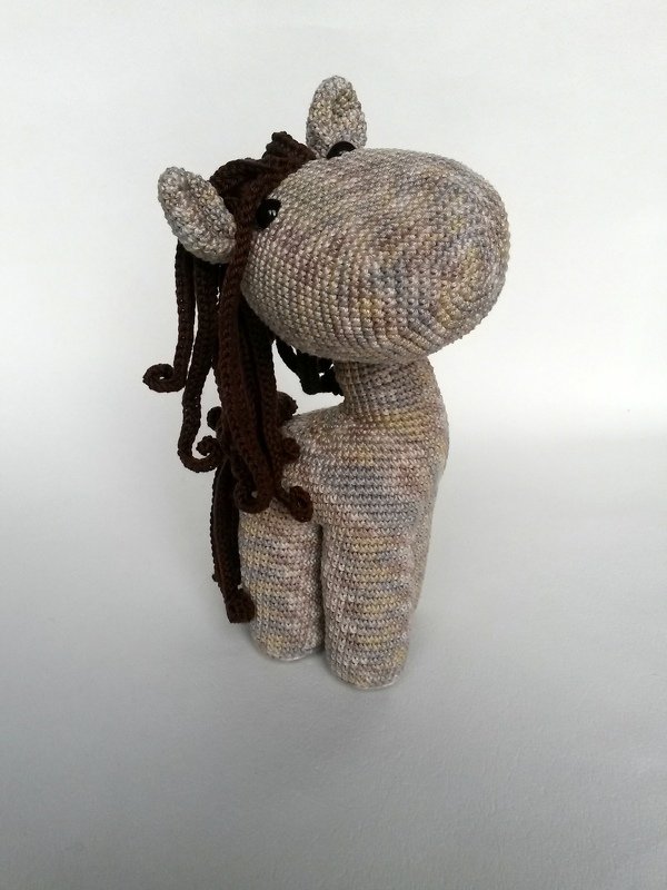 Gehäkeltes Amigurumi-Pferd mit hellem meliertem Körper und brauner Mähne vor weißem Hintergrund