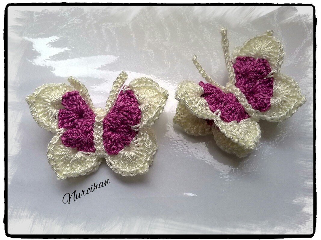 Zwei gehäkelte Schmetterlinge in Creme und Magenta auf heller Fläche