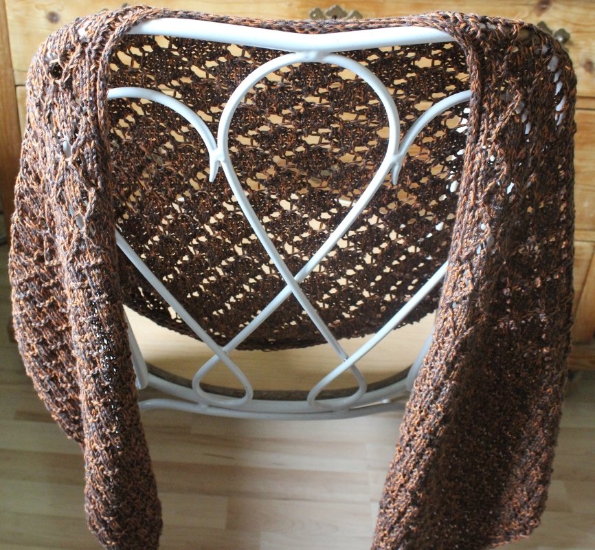 Dunkelbraunes gestricktes Tuch mit Ajourmuster über einem weißen Metallstuhl drapiert.