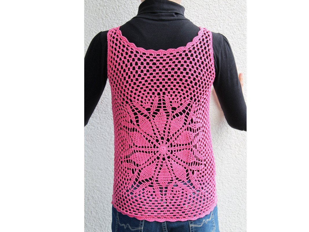 Rückenansicht eines pinken gehäkelten Damen-Tops mit zentralem Blumenmotiv, kombiniert mit schwarzem Langarmshirt.