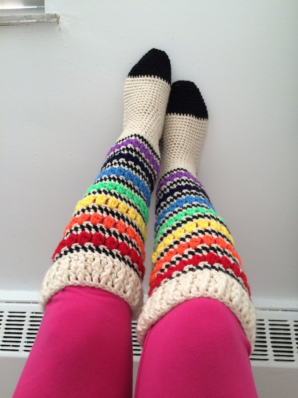 Legs wearing crochet knee-high socks with cream base, rainbow stripes and black toes