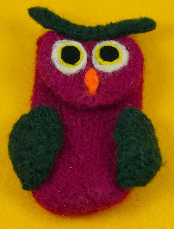 Nahaufnahme einer handgefertigten Strickfilz-Eule in Magenta und Grün auf gelbem Hintergrund