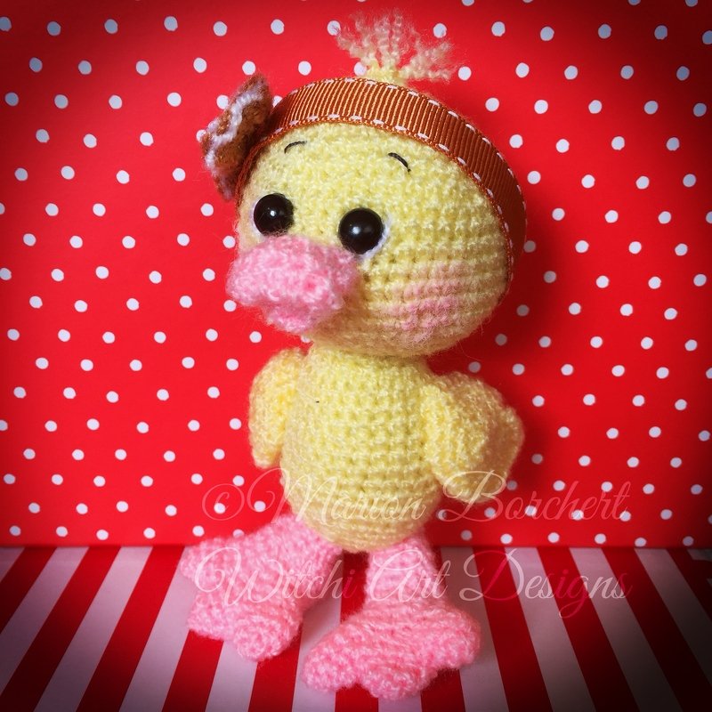 Gehäkeltes gelbes Entenküken-Amigurumi mit rosa Schnabel und rosa Füßen sowie braunem Stirnband