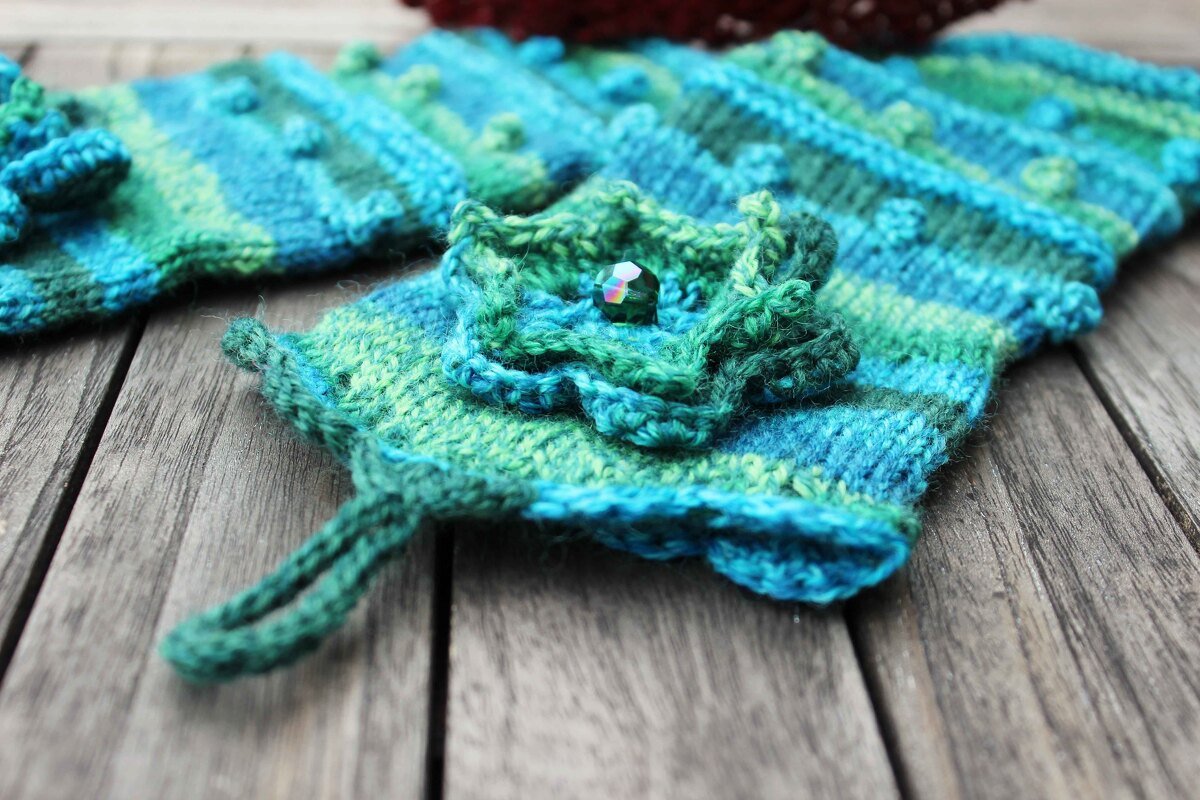 Gestrickte Armstulpen blau-grün mit gestrickter Blüte und Perle auf Holz
