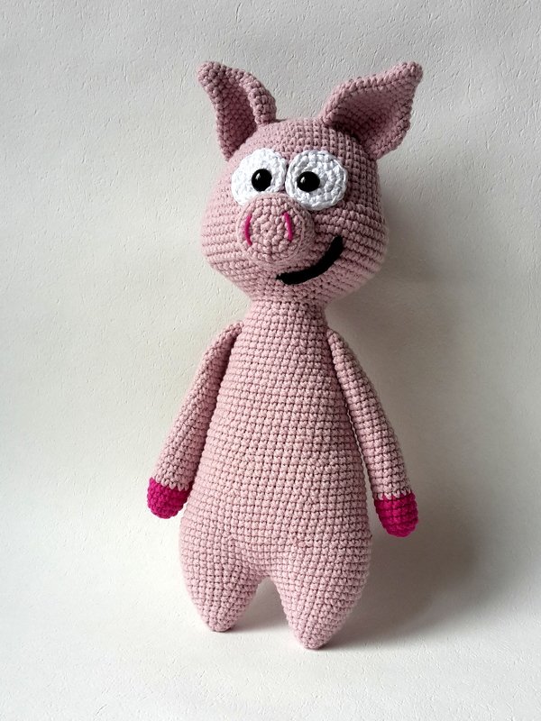Rosa Amigurumi-Schwein mit weißen Augen, schwarzem Mund und pinken Hufen, gehäkelt vor hellem Hintergrund.