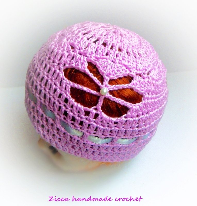 Lilac crocheted baby hat with floral openwork, pearl-style bead and ribbon detail.