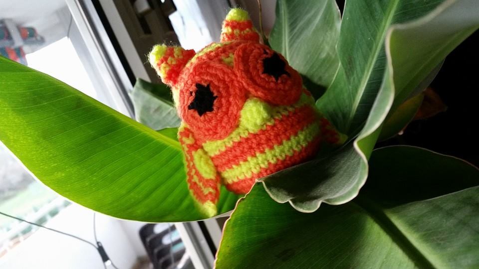 Gehäkelte Eule in Neonorange und Neongrün zwischen grünen Blättern