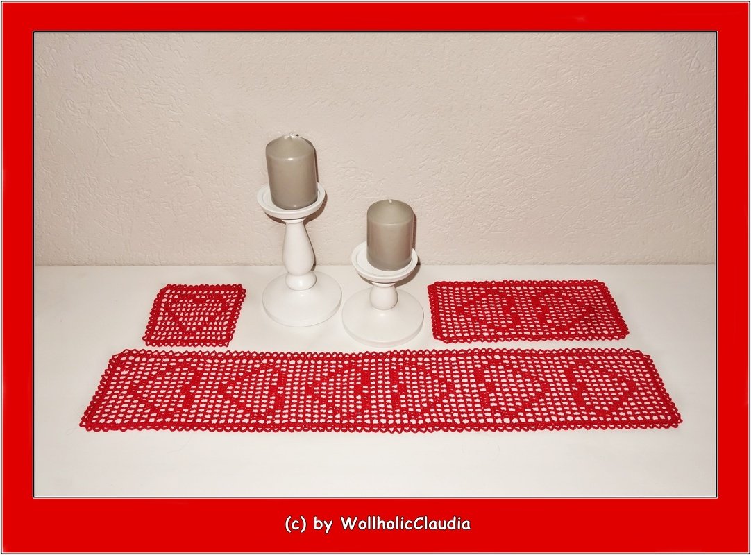 Rotes gehäkeltes Set mit langem Tischläufer, rechteckigem Deckchen und quadratischem Untersetzer mit durchbrochenen Herzmotiven auf weißer Fläche neben zwei weißen Kerzenhaltern mit grauen Kerzen.