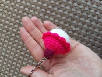 Gehäkelter Cupcake-Schlüsselanhänger rosa, weiß und violett auf offener Hand