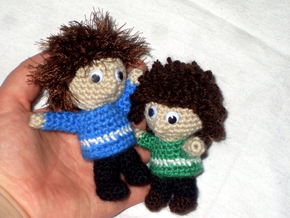 Zwei handgroße gehäkelte Amigurumi-Puppen mit Wackelaugen, blauer und grüner Pullover