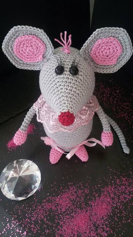 Gehäkelte graue Amigurumi-Maus mit rosa Innenohren, Spitzenkragen, Schleife und roter Nase auf dunklem, glitzerndem Untergrund mit Kristall.