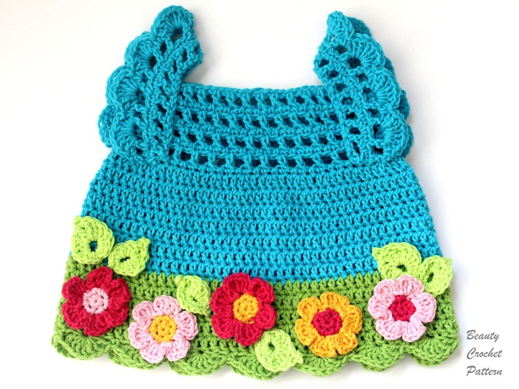 Turquoise crocheted baby dress with a green 'grass' border and colorful 3D flower and leaf appliqués.