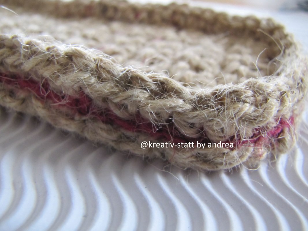 Nahaufnahme eines gehäkelten Korbs aus beiger Naturfaser mit dunkelrosa Streifen