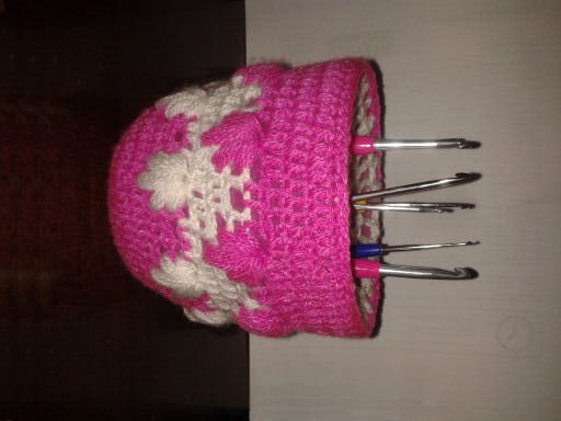 Pinkes gehäkeltes Utensilo mit weißen Schneeflocken, gefüllt mit Häkelnadeln