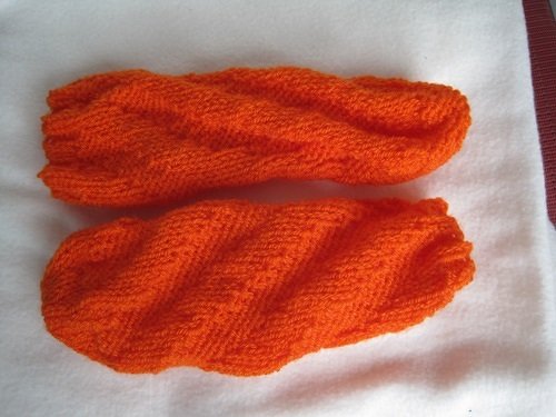 Zwei orangefarbene gestrickte Socken mit diagonalem Strukturmuster auf weißem Untergrund