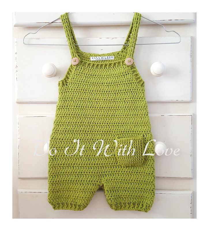 Lindgrüner gehäkelter Baby-Overall mit Trägern, zwei Holzknöpfen und einer kleinen Tasche an einem Drahtbügel