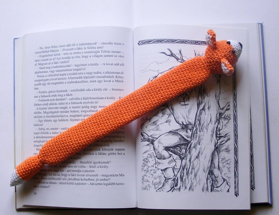 Handgehäkeltes Lesezeichen in Fuchsform (orange und weiß) in einem aufgeschlagenen Buch.
