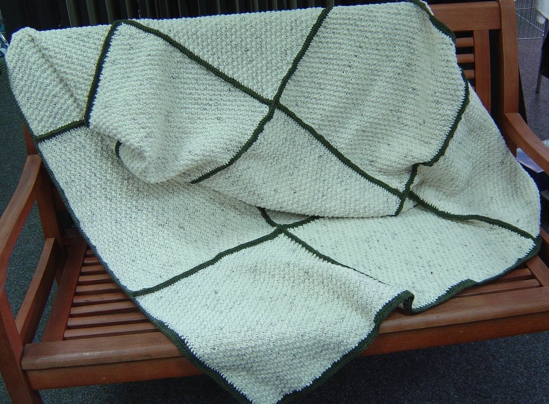 Gestrickte cremeweiße Decke mit dunkelgrünen Linien auf Holzbank