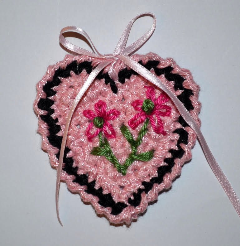 Gehäkeltes rosa Herz mit schwarzem Rand, gestickten pinken Blumen und rosafarbener Satin-Schleife