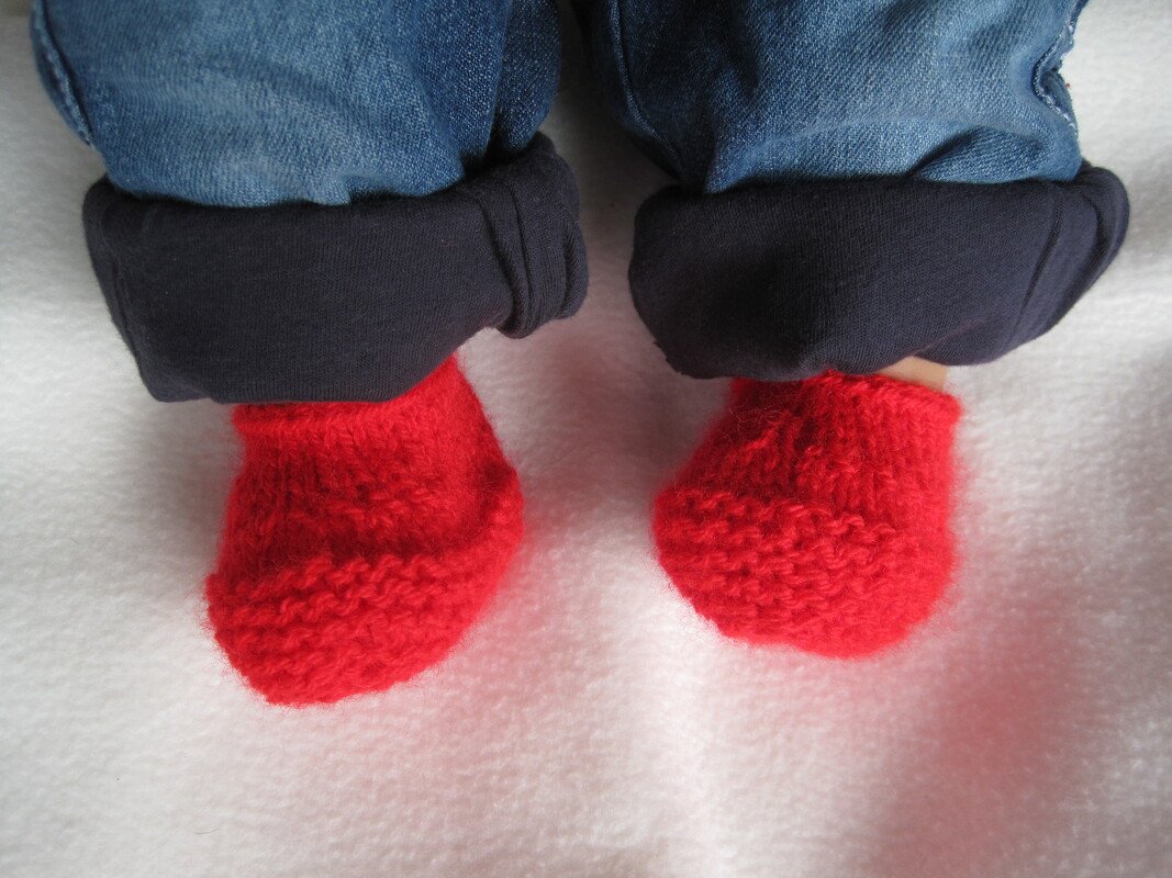 Babyfüße mit roten gestrickten Babyschuhen und umgeschlagener Jeans