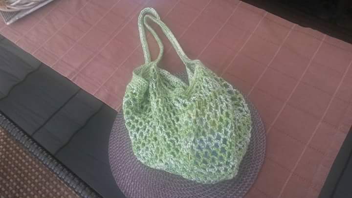 Gehäkelte hellgrüne Netztasche mit zwei Henkeln auf einem runden Platzset