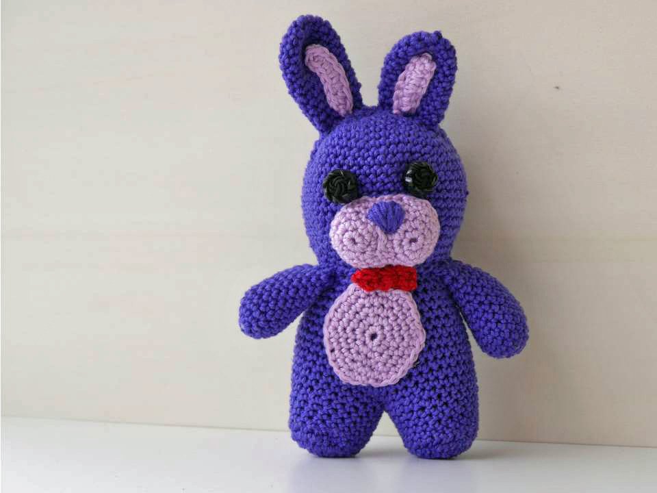 Gehäkelter violetter Amigurumi-Hase mit rosa Bauch und roter Schleife