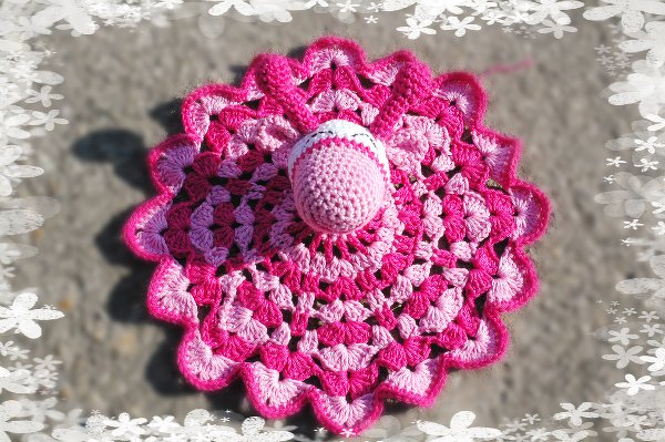 Rundes gehäkeltes Schmusetuch in Pink- und Rosatönen mit gewelltem Rand und kleinem zentralen gehäkelten Element.