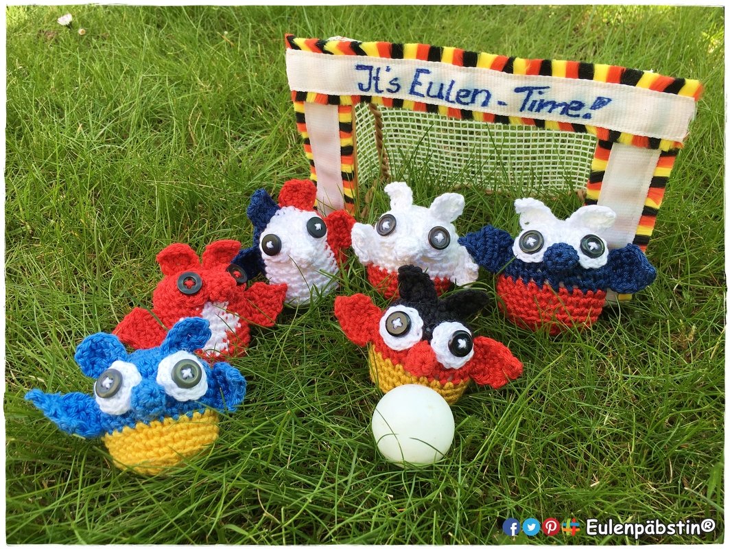 Sechs gehäkelte Eulenfiguren vor Mini-Fußballtor auf Gras mit weißem Ball