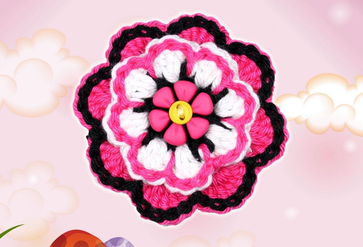 Mehrlagige gehäkelte Blume in Pink, Weiß und Schwarz mit blütenförmigem rosa Element und gelbem Knopf in der Mitte