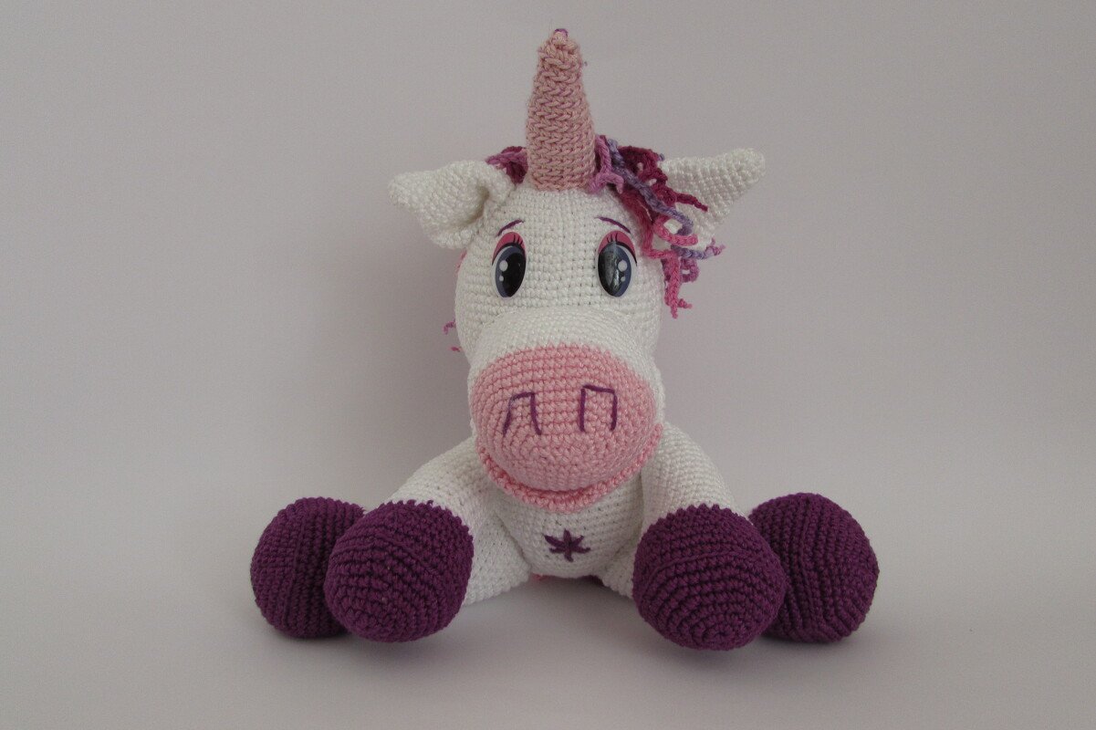 weißes gehäkeltes Einhorn-Amigurumi mit rosa Schnauze und lila Hufen