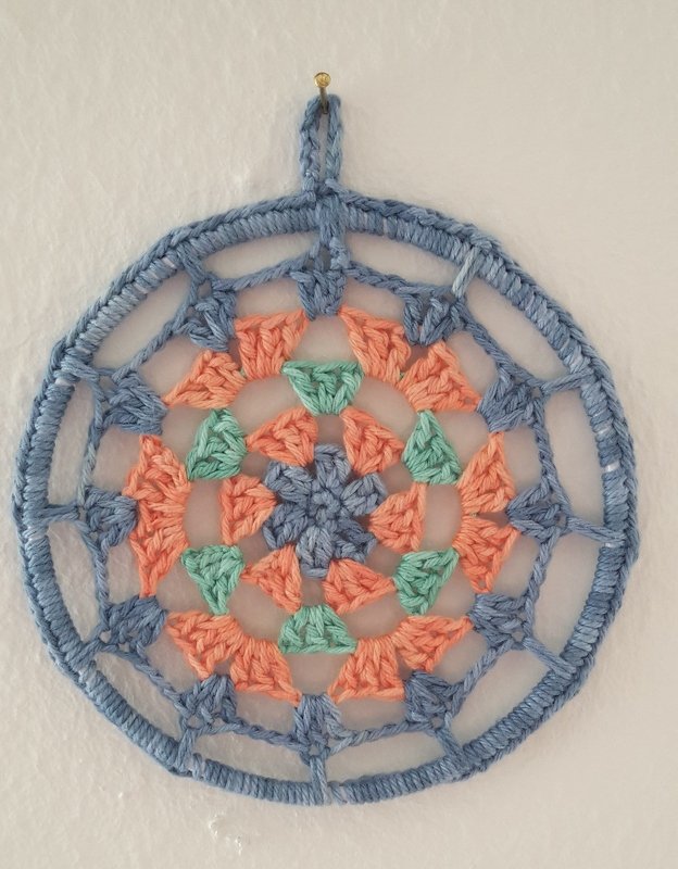 Gehäkeltes rundes Mandala in Blau, Koralle und Mint, an der Wand hängend