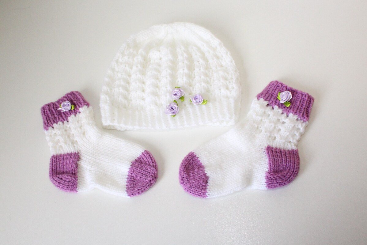 Weiß-lila gestricktes Baby-Set mit Mütze, Socken und kleinen Rosenapplikationen
