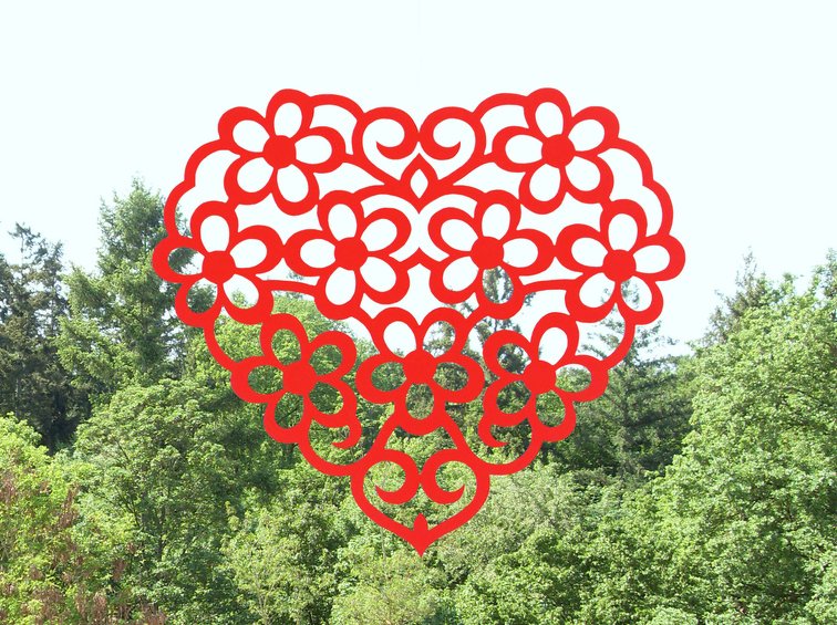 Rotes, filigran geschnittenes Papierherz mit Blumenmotiven vor Bäumen