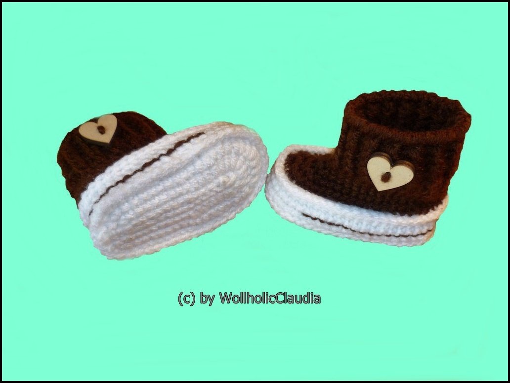 Gehäkelte Babyschuhe in Braun und Weiß mit Herzknöpfen vor mintfarbenem Hintergrund.