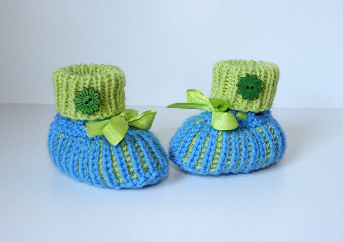 Gestrickte Babyschuhe in Blau und Hellgrün mit Schleifen und blütenförmigen Knöpfen