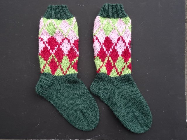 Paar gestrickter Socken mit dunkelgrünem Fuß und mehrfarbigem Rautenmuster in Rot, Rosa und Hellgrün