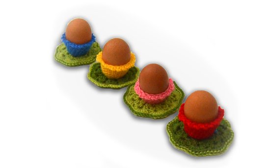 Four brown eggs in colorful crocheted egg cosies on green scalloped mats