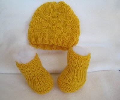 Gestrickte gelbe Babymütze und zwei Babyschühchen mit Strukturmuster auf hellem Hintergrund