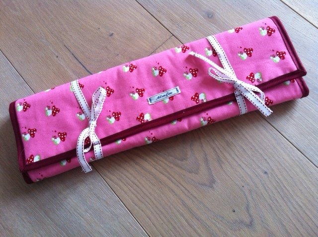 Rosa gerollte Stoff-Aufbewahrungsrolle mit Pilzprint, dunkelrote Einfassung und weiße Bindebänder auf Holzboden