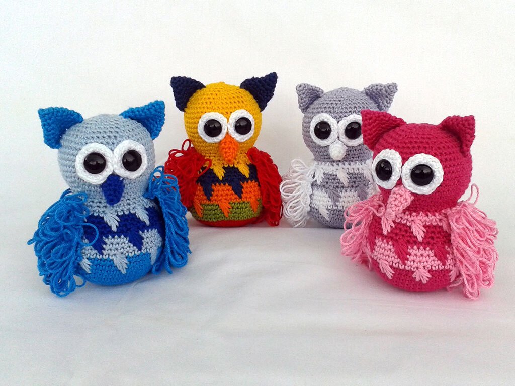 Vier gehäkelte Amigurumi-Eulen in Blau, Gelb, Grau und Pink