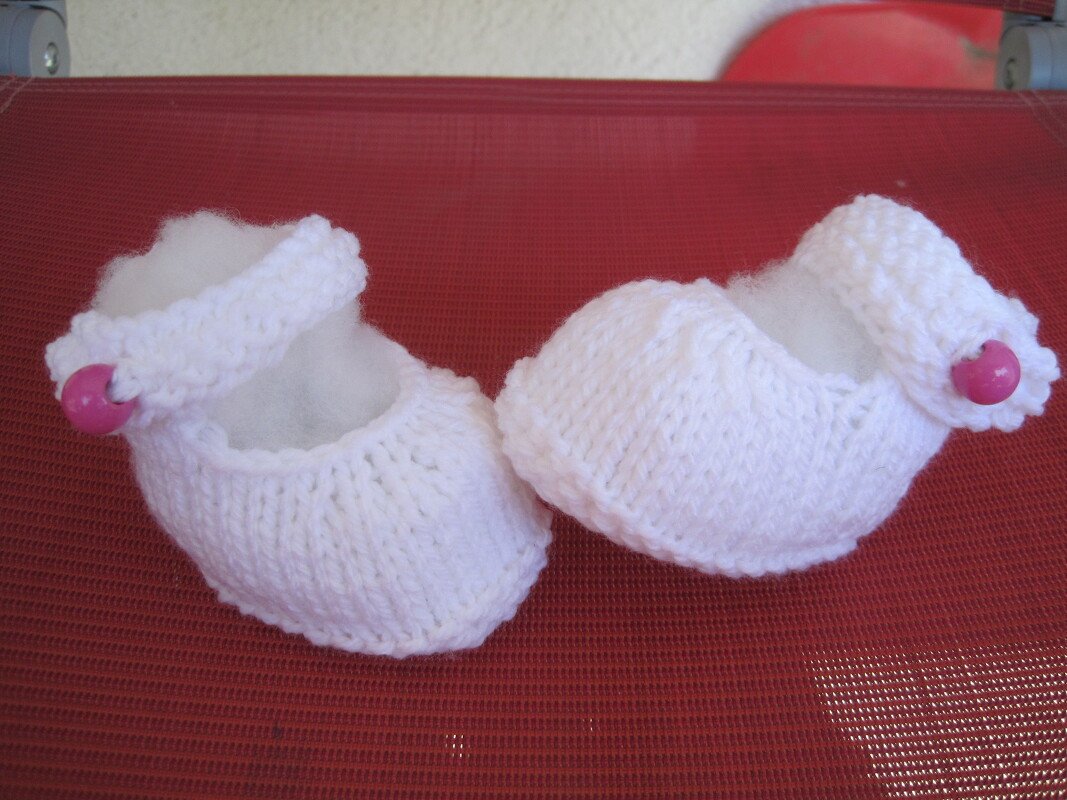 Zwei weiße gestrickte Baby-Ballerinas mit rosa Knöpfen auf rotem Untergrund