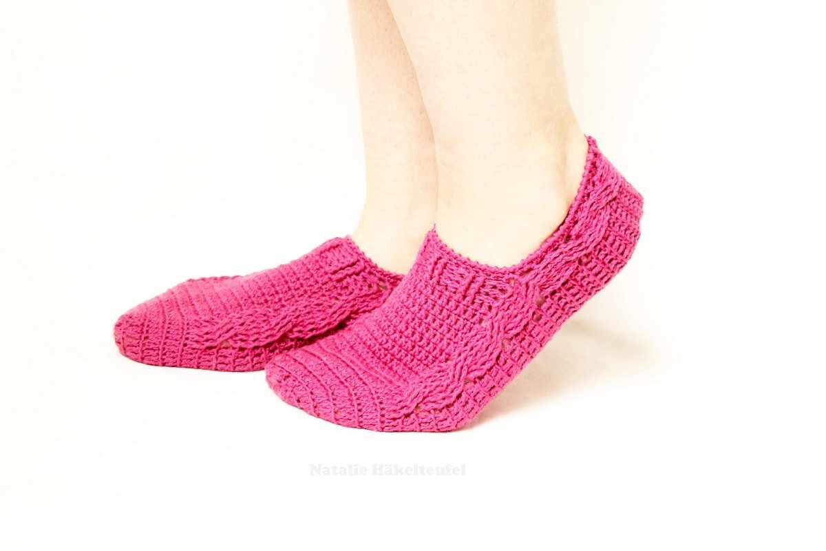 Füße mit rosa, niedrig gehäkelten Socken mit Rippen- und Zopfmuster