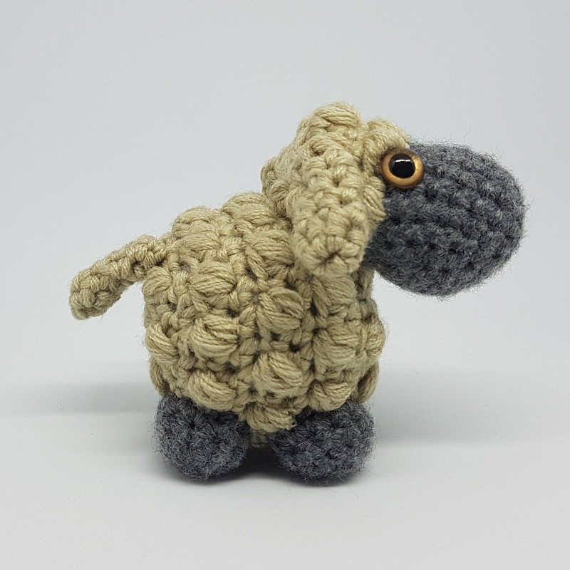 Gehäkeltes Amigurumi-Schaf mit sandfarbenem Noppenmusterkörper und grauem Kopf.