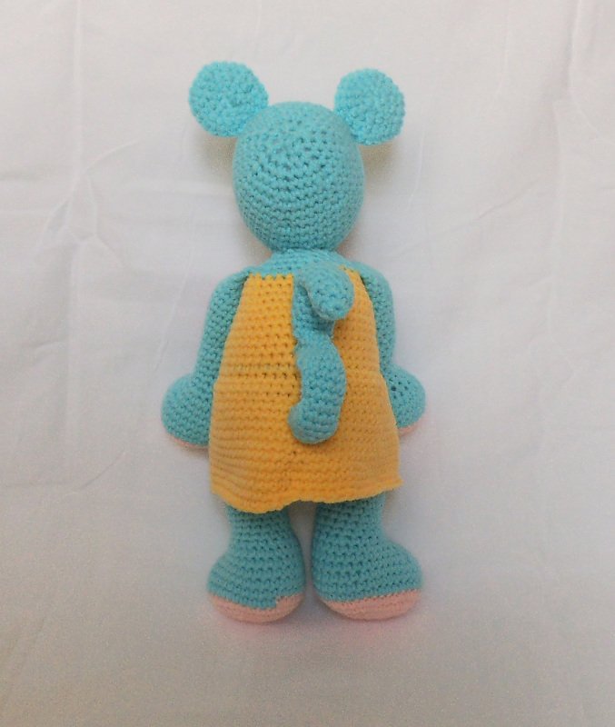 Rückansicht einer hellblauen gehäkelten Amigurumi‑Maus mit gelbem Kleid