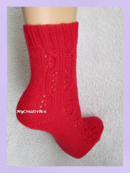 Rote handgestrickte Socke auf Fußform mit Ajour- und Zopfmuster