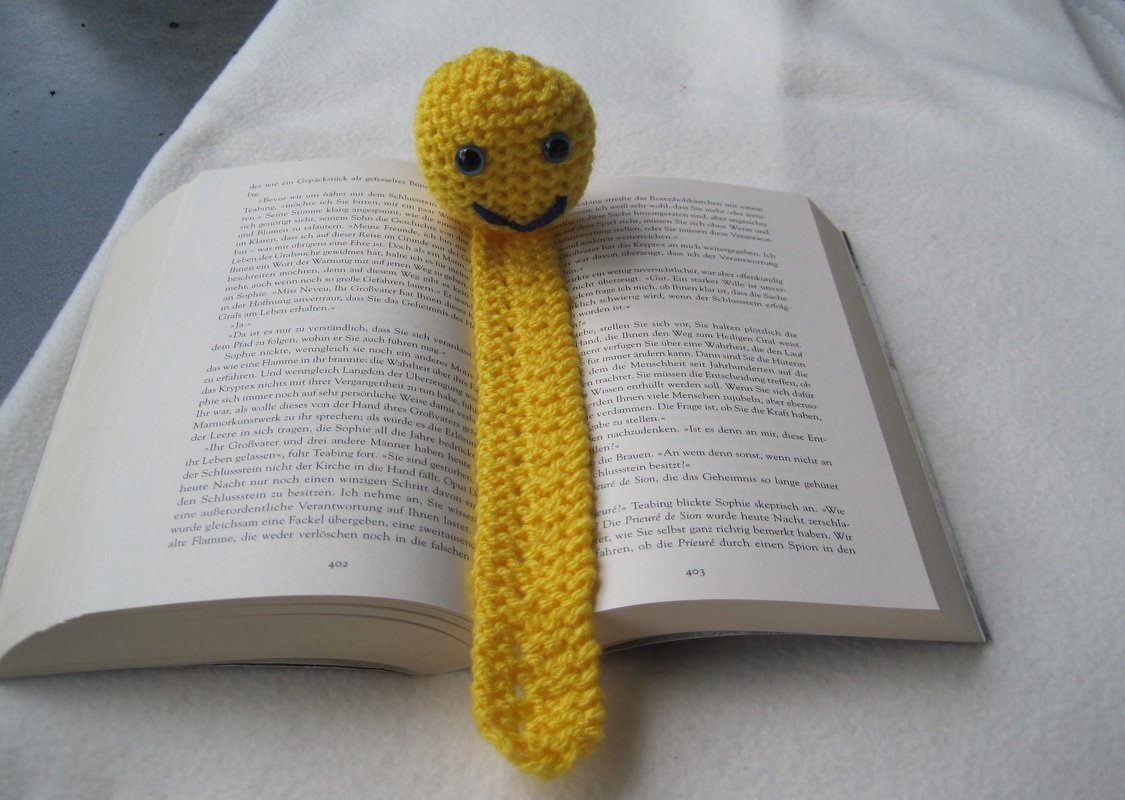 Gelbes gestricktes Lesezeichen mit rundem Smiley-Kopf auf offenem Buch
