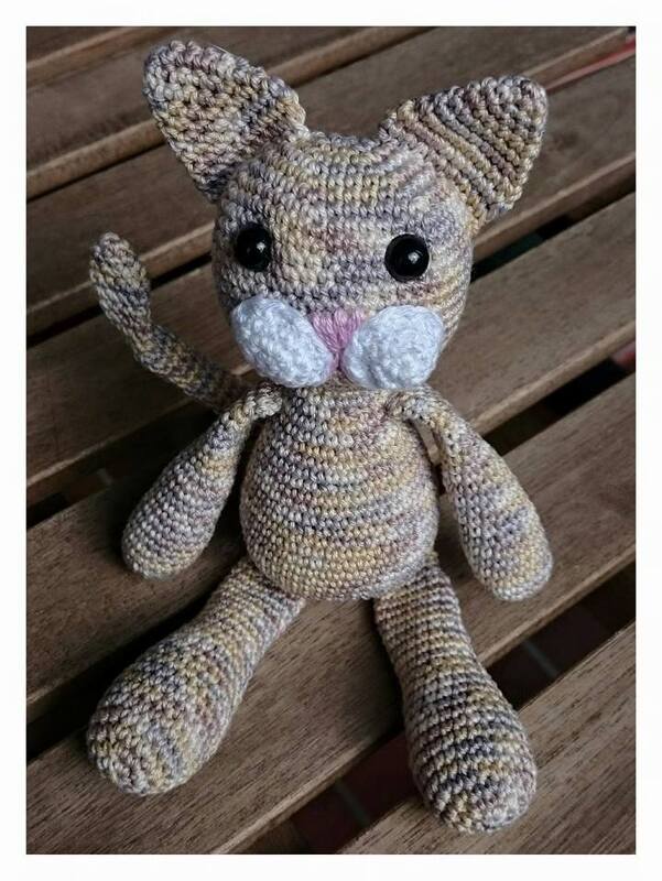 Gehäkelte Amigurumi-Katze mit gestreiftem Garn, weißer Schnauze und schwarzen Augen