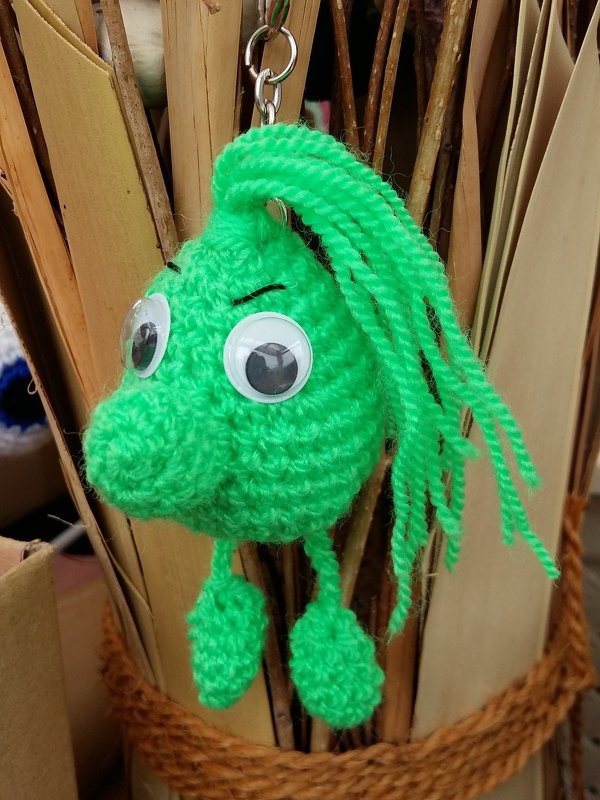 Gehäkelter grüner Amigurumi‑Schlüsselanhänger mit Wackelaugen und Fransenhaar